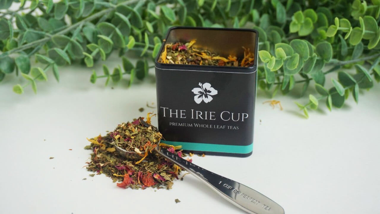 Metal tin of loose leaf tea from The Irie Cup with measuring spoon full of perfect serving size. 