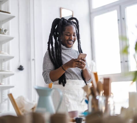 Young Black woman looking at her line of credit on her phone in her pottery studio.