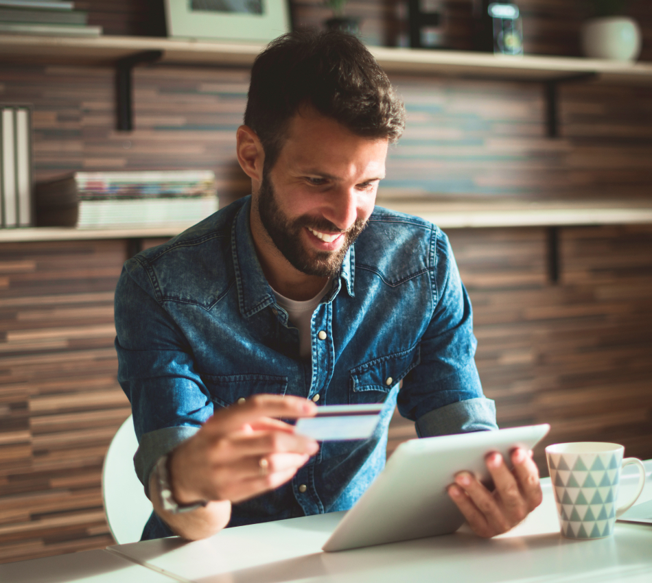 Man smiling at tablet while holding business credit card.