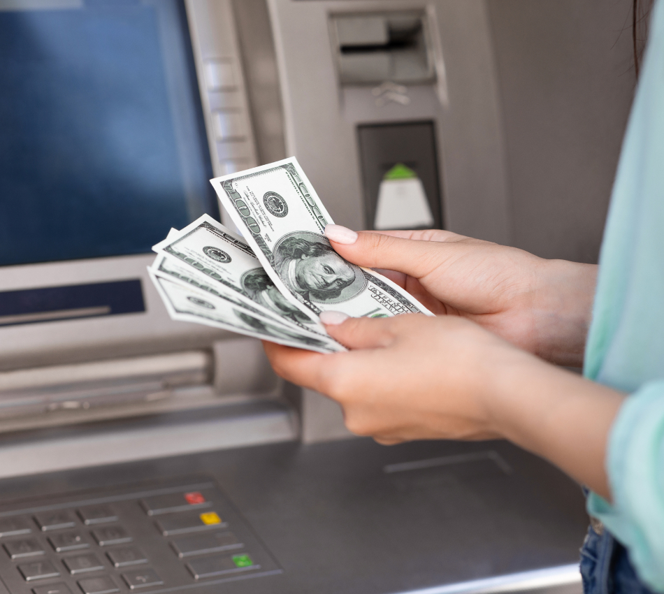 Close-up of woman holding cash next to an ATM.