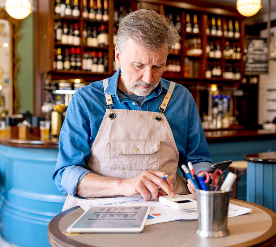 Male bar owner uses a calculator to complete Q4 financial reports.